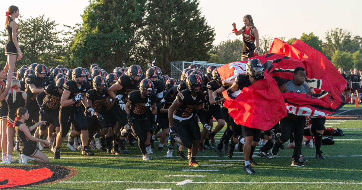 Football team running onto the field through a banner on game night